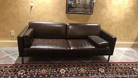 Full front view of brown leather sofa with three seat cushions and chrome legs.