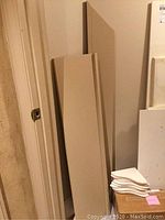 Tan and white wooden shelves of varying sizes leaning against a wall in basement closet.