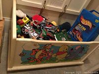 Opened view of the toy chest filled with various toys including Hot Wheels case, toy motorcycles, and other items