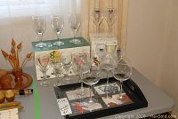 Photo showing 16 clear crystal and glass goblets and wine glasses including some in original boxes, with Umbra branded black photo tray beneath.