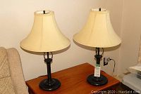 Pair of lamps on wooden table, black metal bases, cream fabric shades with some wear.