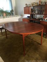 Oval dining table in warm brown teak finish shown from front angle
