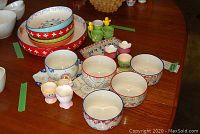 Four colorful stoneware serving bowls, six ceramic egg cups and three trays displayed on wooden table
