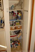 Photo of pantry cabinet shelves showing various kitchen items including plastic food containers, cleaning sprays, canned and boxed food, baskets with wraps and utensils.