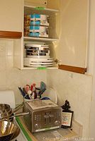 Photo showing Cuisinart 4-slice toaster on countertop with assorted utensils in blue container next to it, metal colander beside, and ceramic utensil crock.