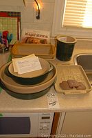 Full view of Pampered Chef ceramic bakeware including round and oval dishes, loaf pan, crock, cookie molds, and cookbook arranged on kitchen counter.