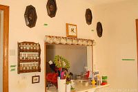 Wide view of kitchen pass-through area showing spice rack with jars, hanging ceramic mugs, kitchen utensils, and wall decorations.