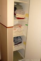 Closet with multiple shelves filled with folded linens including sheets, duvet covers, and bedspreads in various colors and patterns.