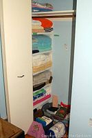 Closet shelves filled with stacks of bath and hand towels in various colors and a few bath mats visible.