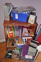 Overview of multiple office supplies arranged on a wooden shelf including folders, stationery, and storage boxes