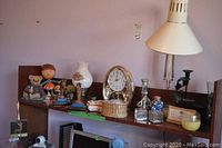 Wide view of shelf with desk lamp, clock, various figurines, glass bottles, and candle