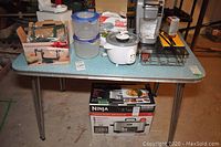 Front angle view of retro kitchen table showing chrome legs, laminate top, and extendable leaf folded down. Several kitchen items placed on table to show scale.