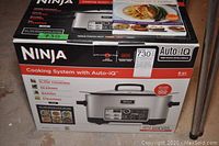 Box of Ninja Cooking System with Auto-IQ, showing product image and features such as slow cooking, searing, baking, steaming, with 6 quart capacity.