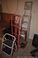 Photo showing the full assortment of tools including 6 ft aluminum painter's ladder, 4 ft white metal step ladder, wooden saw horse, small wooden step, and heavy duty steel dolly with red handles.