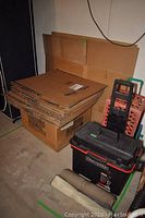 Photo showing stacked flat cardboard boxes on top of a large box, beside a Craftsman tool chest, luggage carrier, and milk crates.