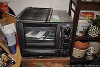 Wolfgang Puck convection oven with wire rack and baking tray placed on top, positioned among various kitchen items.