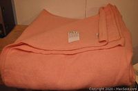 Folded peach-colored wool blanket with a label attached.