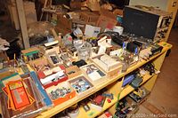 Overview of multiple small boxes with electronic parts, hardware, and some circuit boards on shelves.
