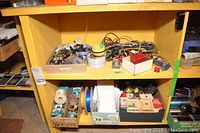 Overview of two yellow shelves with multiple boxes and bins filled with wires, tape rolls, and various electrical hardware parts.