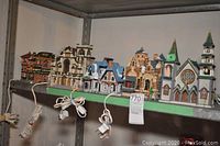 Row of five ceramic or resin Christmas village buildings including a police station, houses, and church, all with light cords attached
