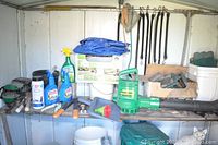 Wide view of the garden supplies including sprays, shoe aerators, a box of garden edging, a leaf blower, and various garden tools on a shed shelf.