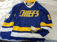 Blue Charlestown Chiefs hockey jersey with yellow and white stripes, featuring number 18 on sleeves laid flat.