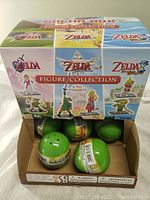 Box showing six factory sealed egg-shaped green collectible packs featuring The Legend of Zelda character figures from various Zelda titles.