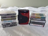 Photo of red GE cassette Walkman player with built-in speaker and radio tuner, displayed alongside nine cassette tapes featuring various artists.
