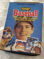 Blue box with smiling baseball player and sample baseball cards on front, signed image printed on box.