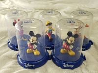 Front view showing all six Disney character figurines enclosed in individual clear plastic domes with blue Disney bases