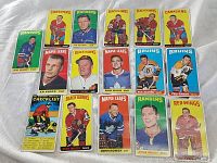 Top view of 17 individual 1964 Topps Tall Boys hockey cards laid out on gray fabric, showing players from Canadiens, Rangers, Black Hawks, Maple Leafs, Bruins and Red Wings teams with colorful backgrounds.