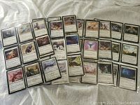 Collection of Magic the Gathering cards laid out, showing multiple cards in sleeves on fabric background.