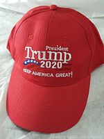 Front view of red baseball cap with embroidered President Trump 2020 campaign text and slogan