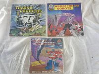 Three transformers and gobots themed music books shown on fabric background.