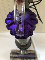 Close-up top-down photo of the Dyson vacuum showing the purple cyclone dome with '2 tier radial cyclones' printed and clear dustbin below.