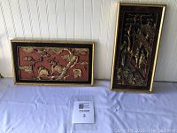 Two Asian plaques side by side on a white surface against beadboard wall, one horizontal and one vertical.