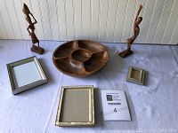 Lot arranged on light surface against beadboard wall showing two African-American wooden figurines standing on either side of the solid wood Lazy Susan with four compartments. Four assorted picture frames are placed around them.