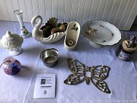 Overview of the lot items displayed on a blue cloth, showing the Lenox swan centerpiece, candle holders, trivet, and other decorative china pieces.