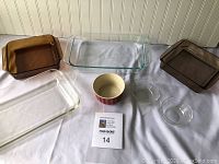 Lot of Pyrex and CorningWare bakeware on white cloth surface including various glass baking dishes and ramekins.