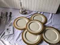 Five vintage off-white ceramic plates with wide gold rims arranged on a cloth surface.