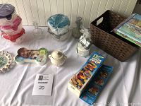 Wide shot of all items on a white tablecloth including Jenga game boxed set, plastic containers, dog bone picture, beige ceramic candle holder, two glass bottles with stoppers, and brown woven basket with books.