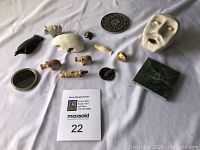 Photo of assorted tchotchkes and collectibles arranged on white fabric, showing stone animals including a polar bear, black bird, hippopotamus, decorative coaster with Bell Telephone logo, carved mask, small mirror, and a green box.