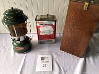 Full lot of vintage Coleman lantern, fuel canister, and wooden box arranged on white surface with auction card shown