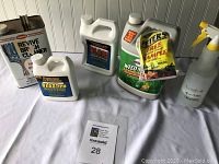 Photo showing assorted household chemicals including Revive Brush Cleaner in a metal can, Blast PM Block Cleaner bottle, Drain Opener jug, Vegetation control weed stop, and a spray bottle.