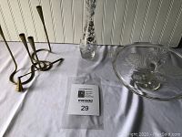 Photo of brass candlestick holder with three arms, the brass candle snuffer, tall glass vase with floral design, large glass round serving dish with peacock decoration