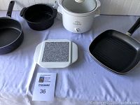 Full view of assorted cookware and small crockpot including cast iron skillets, non-stick pan, ceramic trivet, and Rival Crock-Pot.