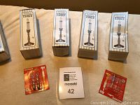 Five boxed pewter electric window candles and two packs of replacement bulbs with a MaxSold catalog card in front.