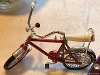 Close up photo of miniature red bicycle Christmas ornament showing white grips and black pedal details.