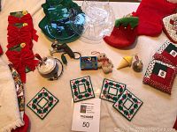 View of assorted Christmas ornaments and decorations laid out on beige surface, showing bows, fabric stockings, coasters, tree dish, and figurines