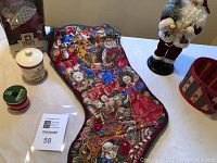 Photo showing the oversized Christmas stocking with detailed holiday images and the Santa Claus figurine, along with jar, ribbon, and basket.